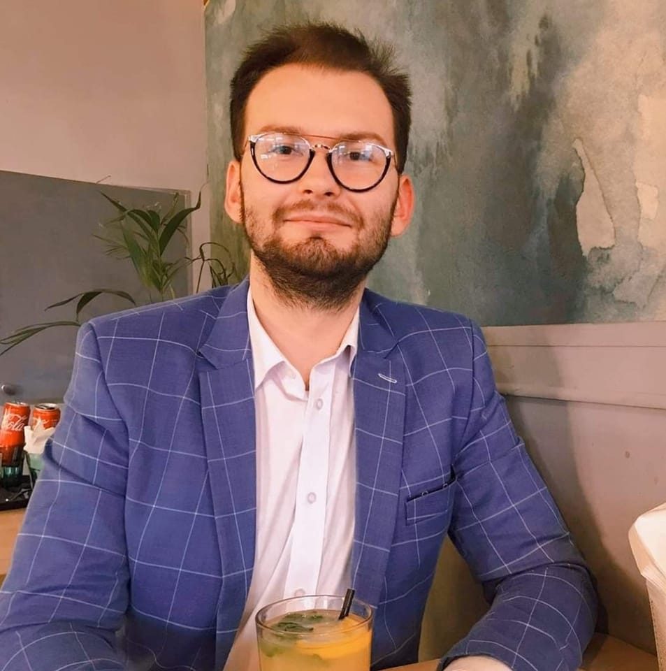 Mężczyzna w okularach i niebieskiej marynarce siedzi przy stole z drink