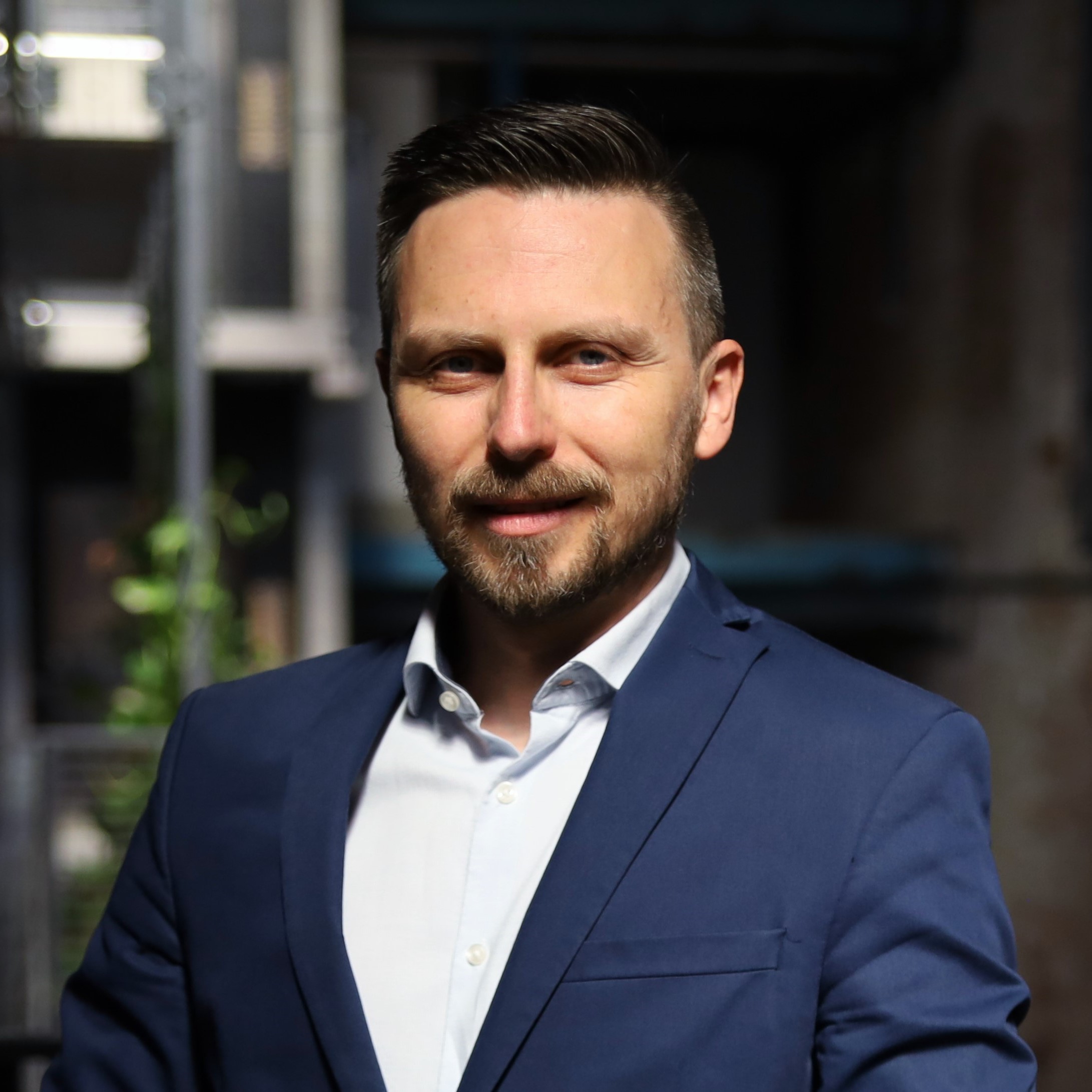 Profesjonalny portret mężczyzny w niebieskiej marynarce i białej koszuli na tle budynku.