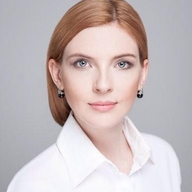 Portret profesjonalnej kobiety z rudymi włosami w białej koszuli na szarym tle.