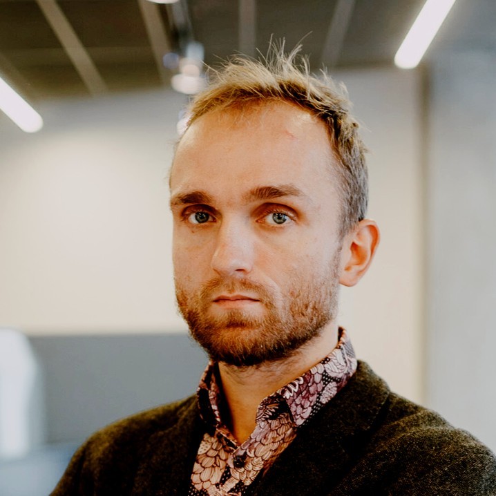 Portret mężczyzny z rudymi włosami i brodą w biurze, patrzy w kamerę