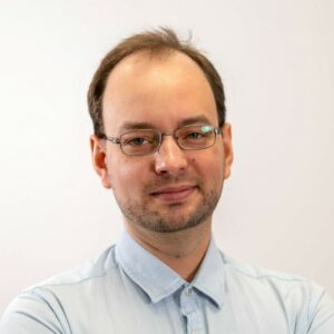 Portret profesjonalnego mężczyzny w okularach i błękitnej koszuli na białym tle.