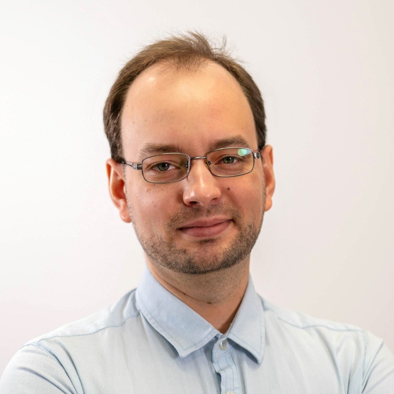 Portret profesjonalnego mężczyzny w okularach i błękitnej koszuli na białym tle.
