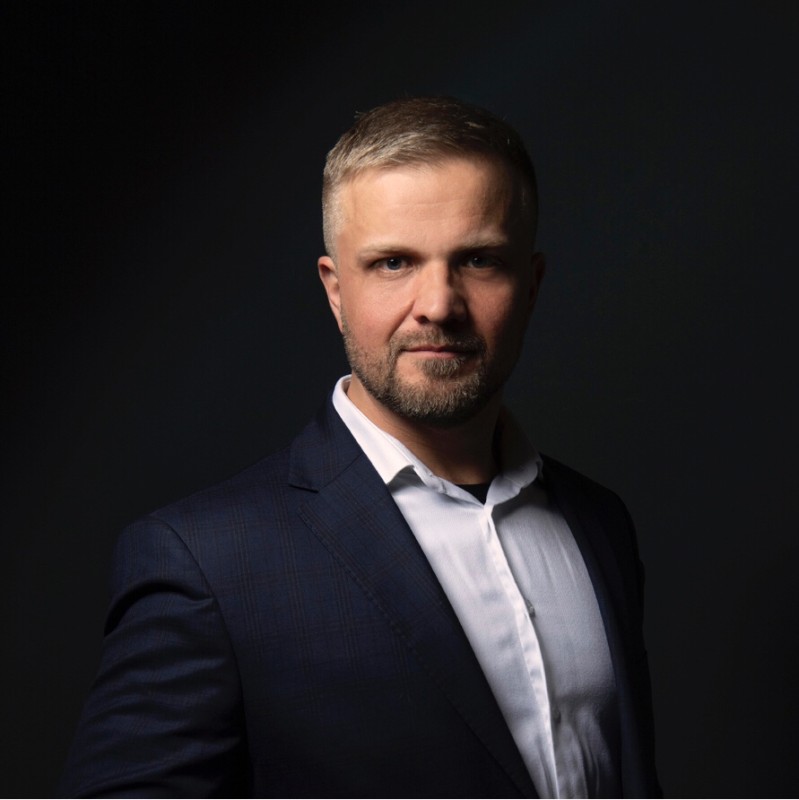 Portret profesjonalny mężczyzny w ciemnym garniturze i białej koszuli na czarnym tle.
