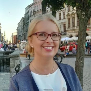 Uśmiechnięta kobieta w okularach na tle europejskiego miasta z historycznymi budynkami