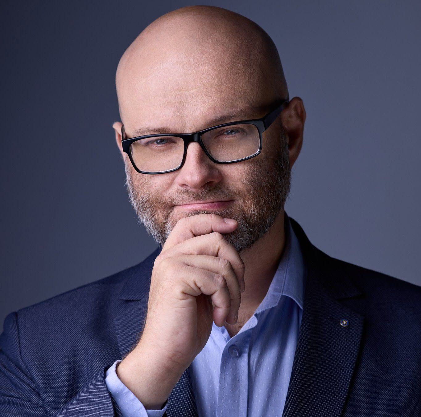Łysy mężczyzna w okularach i garniturze, myślący, profesjonalny portret biznesowy.