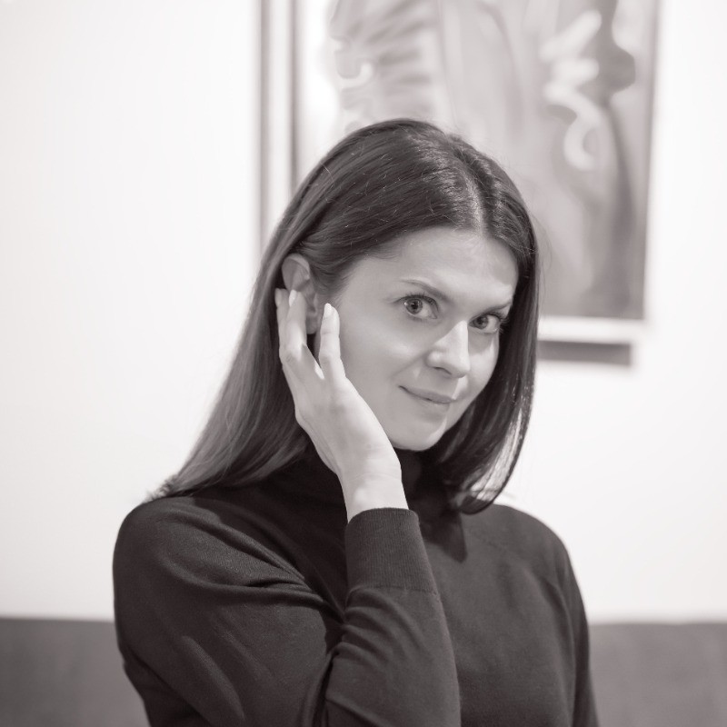 Portret kobiety z długimi czarnymi włosami, ręką przy twarzy, w czarnej bluzce, czarno-białe zdjęcie.