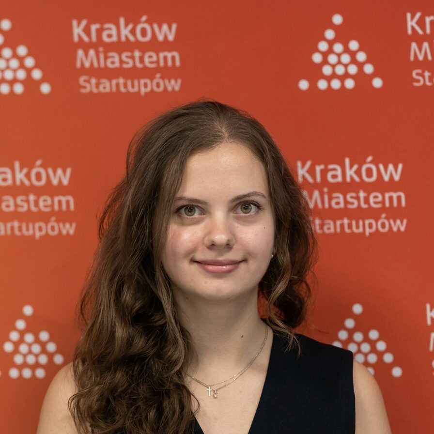 Portret młodej kobiety na tle czerwonego baneru Kraków Miastem Startupów