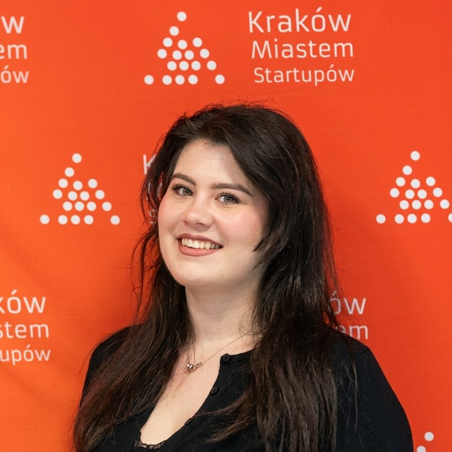 Kobieta na tle logo Kraków Miastem Startupów podczas konferencji biznesowej