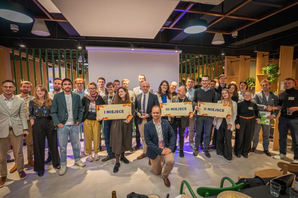 Grupa ludzi pozuje ze znakami I MIEJSCE, II MIEJSCE, III MIEJSCE podczas ceremonii wręczenia nagród w nowoczesnym wnętrzu.
